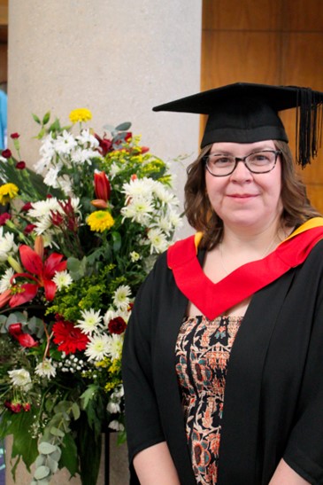 A graduate standing beside flowers in her graduation gown