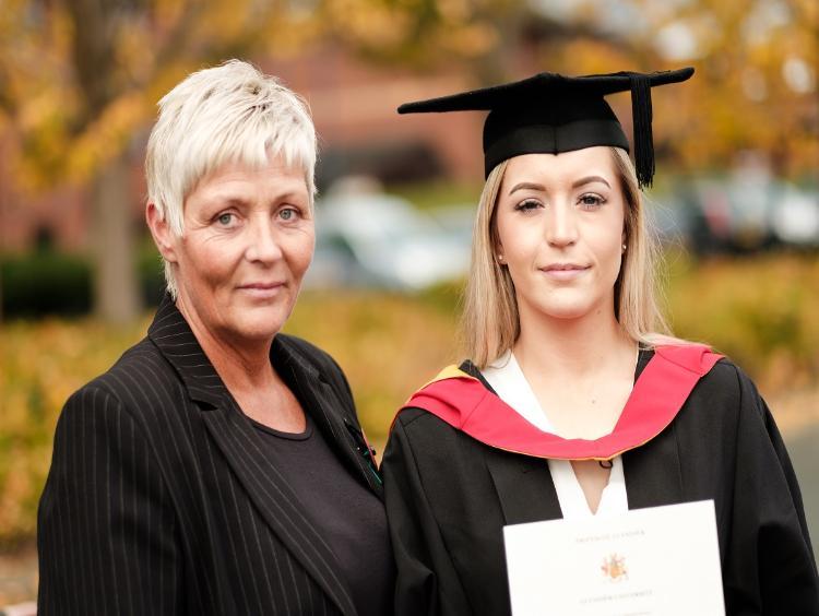 A graduate in cap and gown holding a certificate