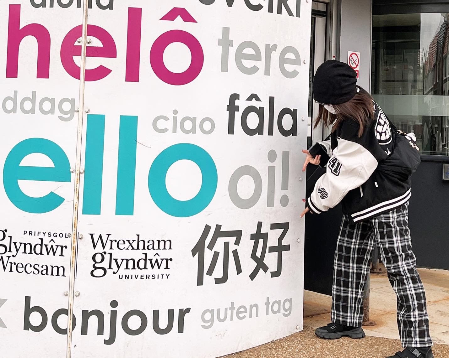 student pointing at chinese characters for hello outside a building