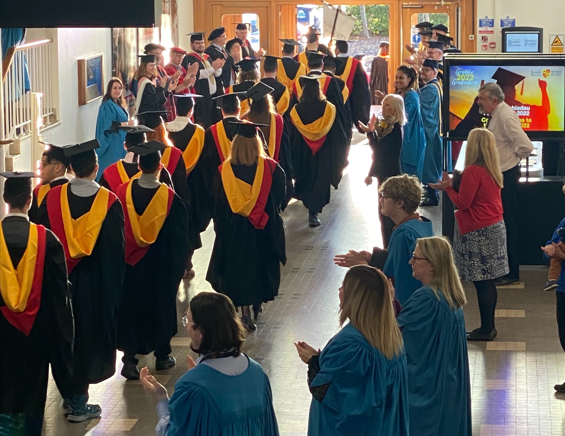 students walking through reception in cap and gowns