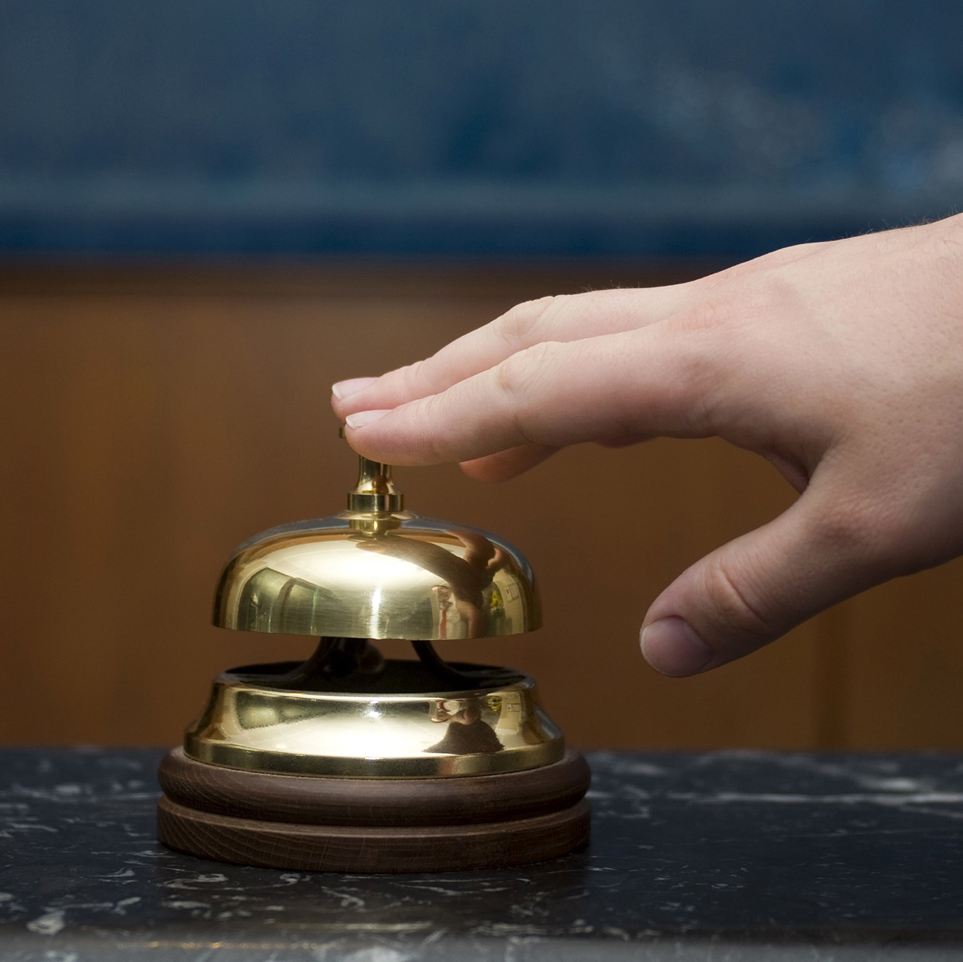 A hand reaches out to ring a service bell on a desk
