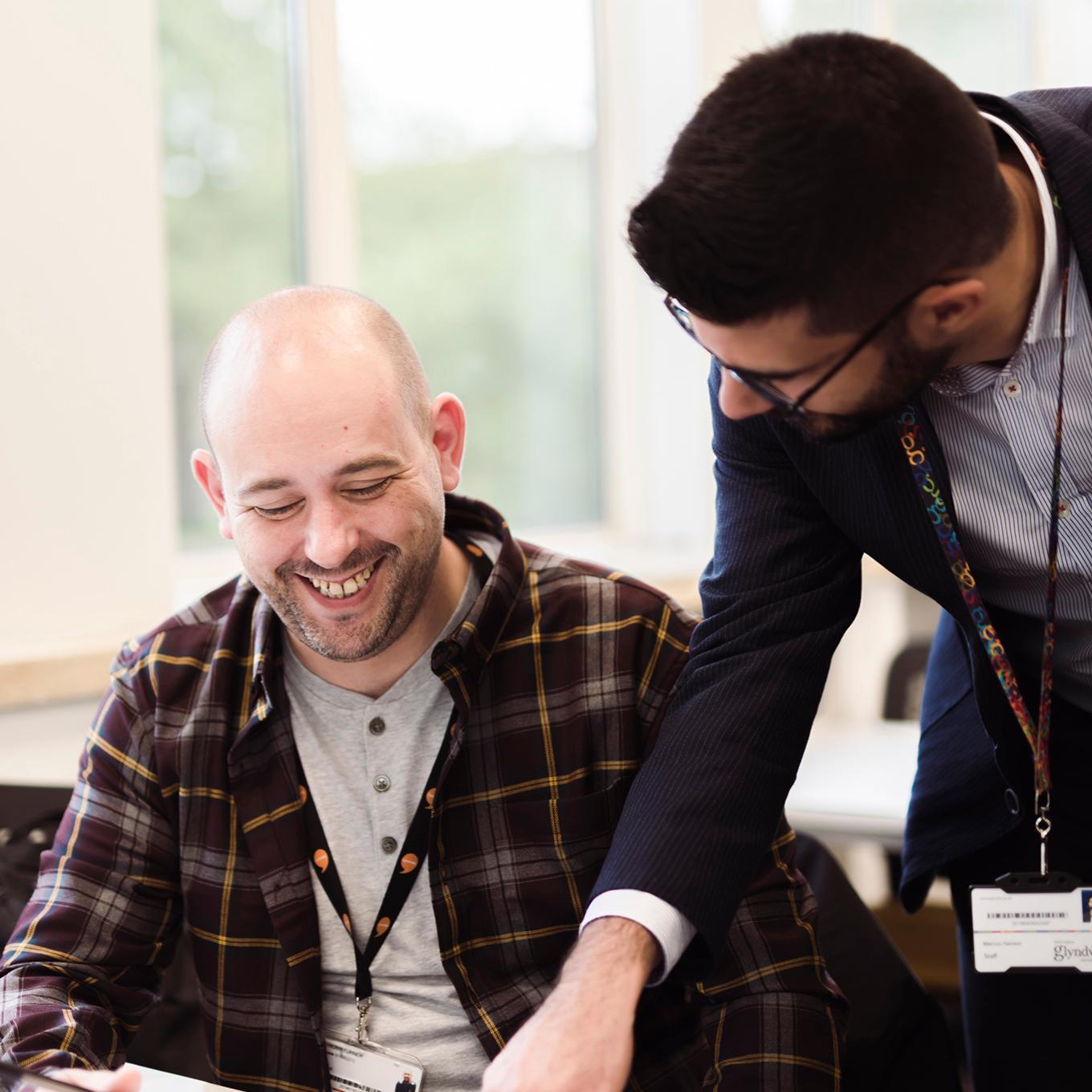 A student is smiling as the lecturer explains something to them. The lecturer is pointing at the work on the desk.