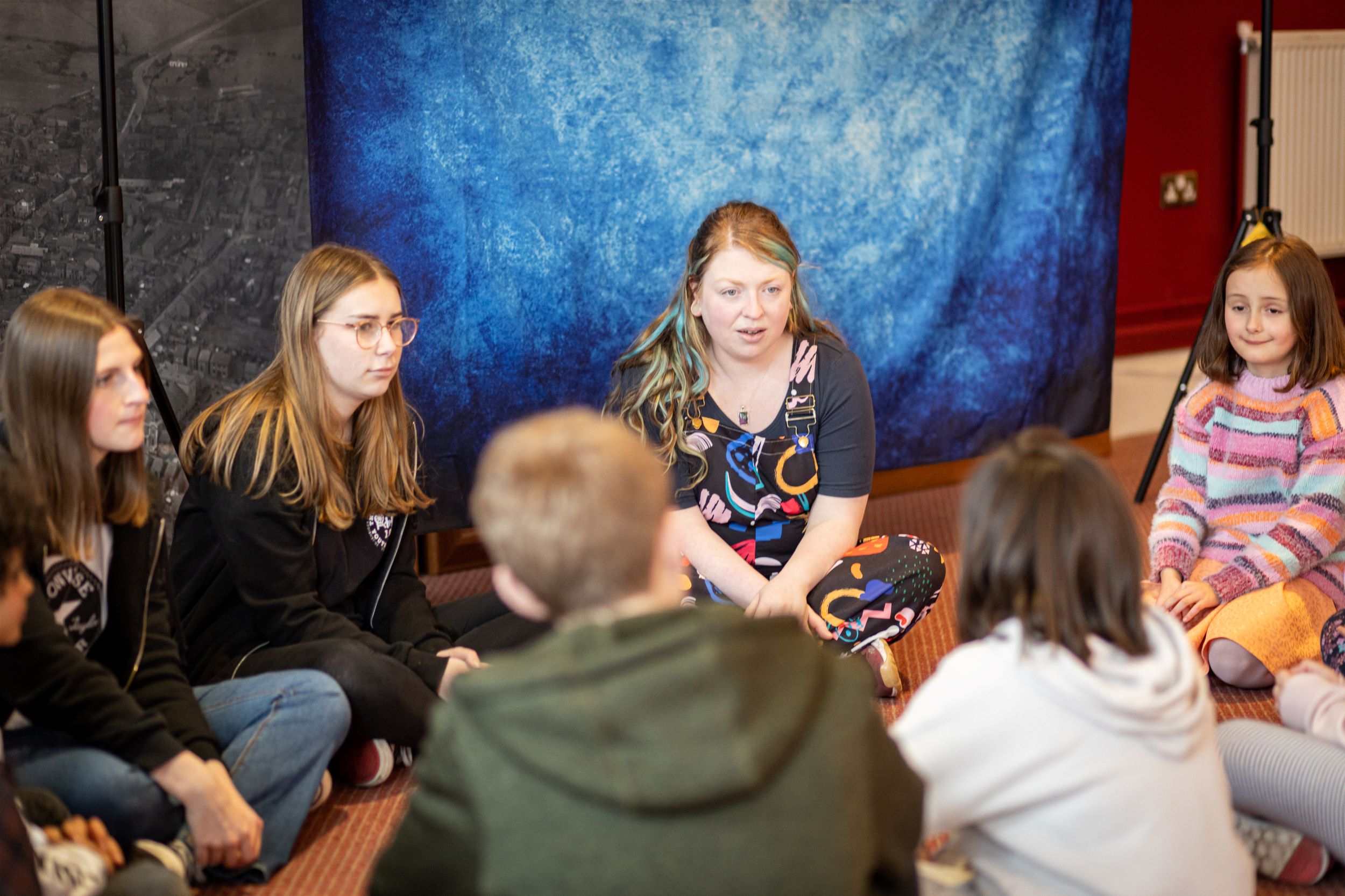 Kids sat around a teacher in a drama workshop