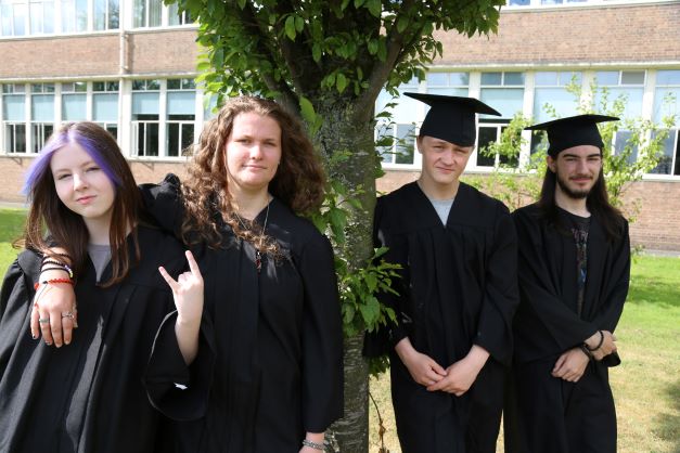 Teenagers in graduation gowns by a tree