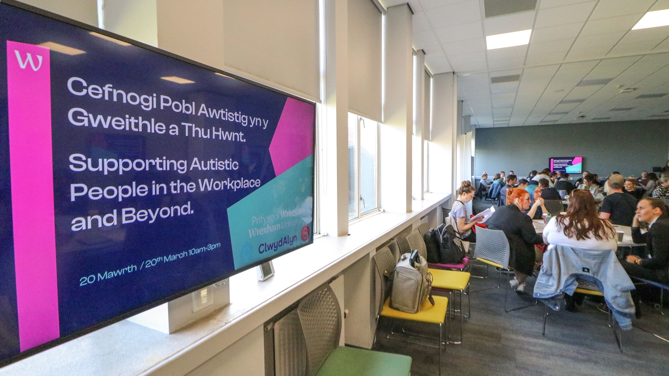 A group of people at a conference with a presentation on screen saying Supporting Autistic People in the Workplace