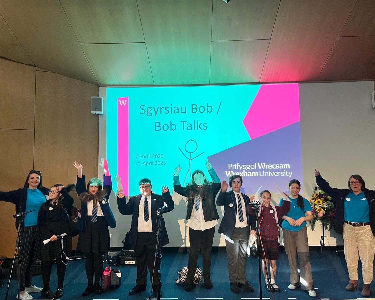 A group of young people celebrating on stage whilst in front of a presentation slide that says Bob Talks.