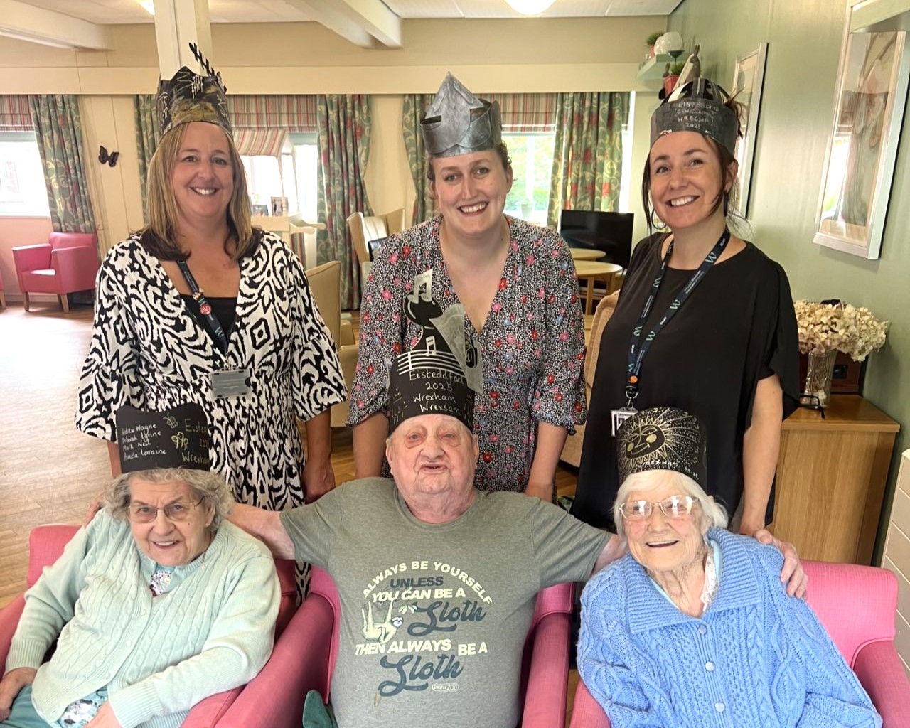 A group of people from care homes and civic mission staff together for a photograph. They are wearing Eisteddfod crowns crafted by themselves.