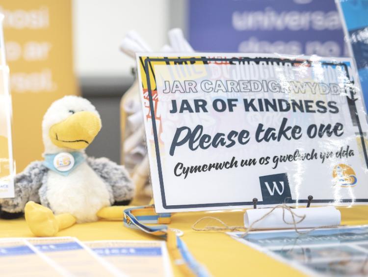 A teddy version of a seagull on a desk with a sign next to it that says Jar of Kindness, please take one.