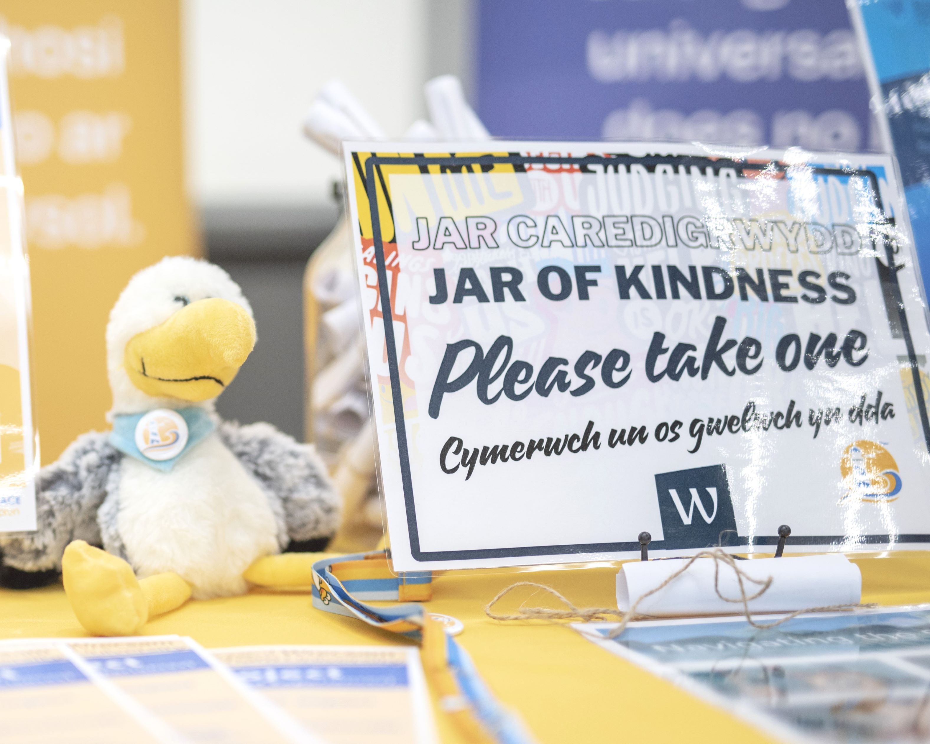A teddy version of a seagull on a desk with a sign next to it that says Jar of Kindness, please take one.