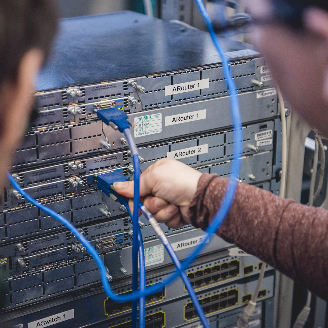 Two students face a server stack, one plugs in a cable