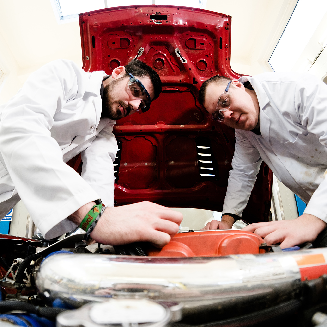 Two students wearing safety goggles working under the bonnet of a car