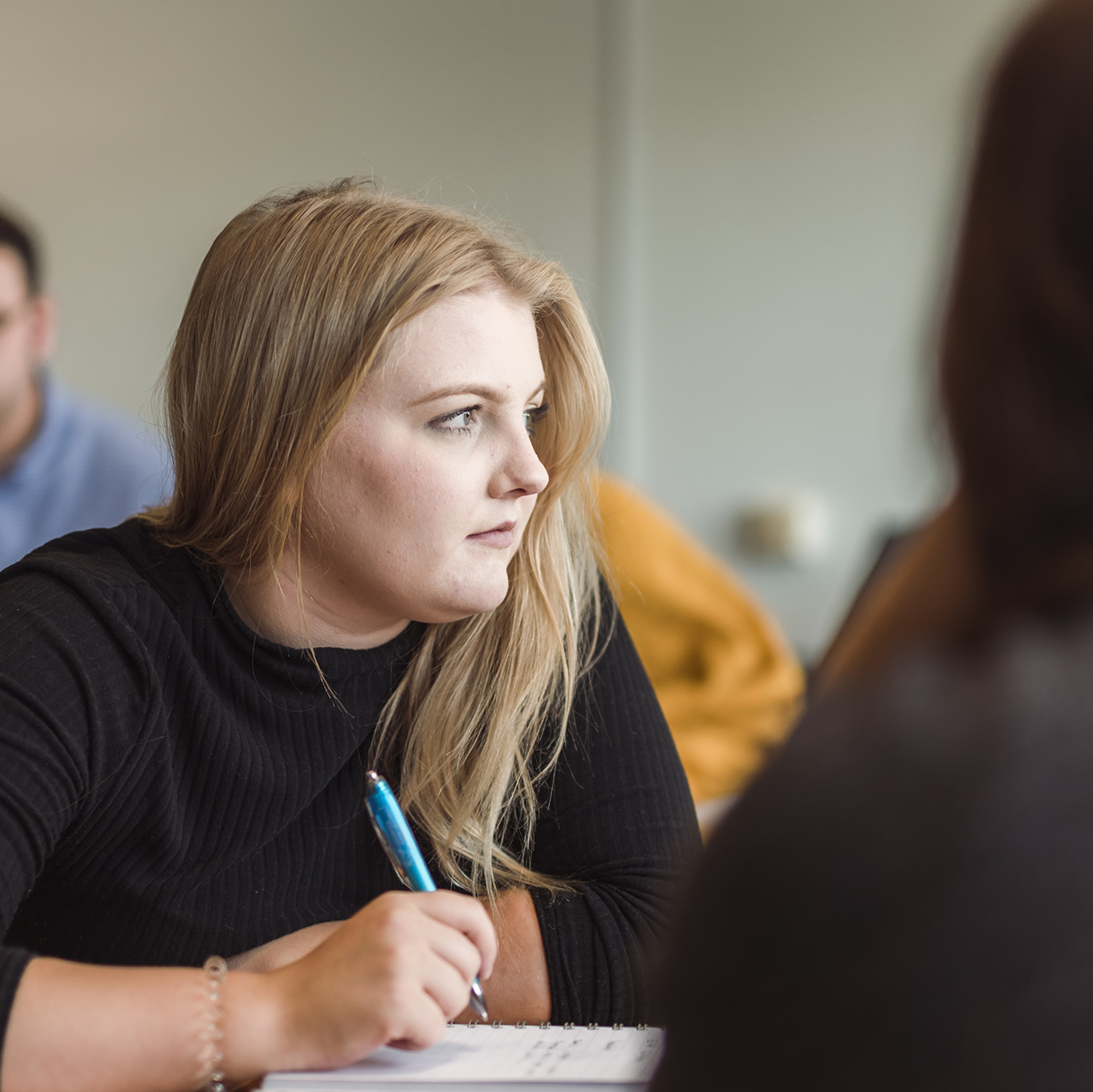 A student looks to the side, her pen poised over her notebook