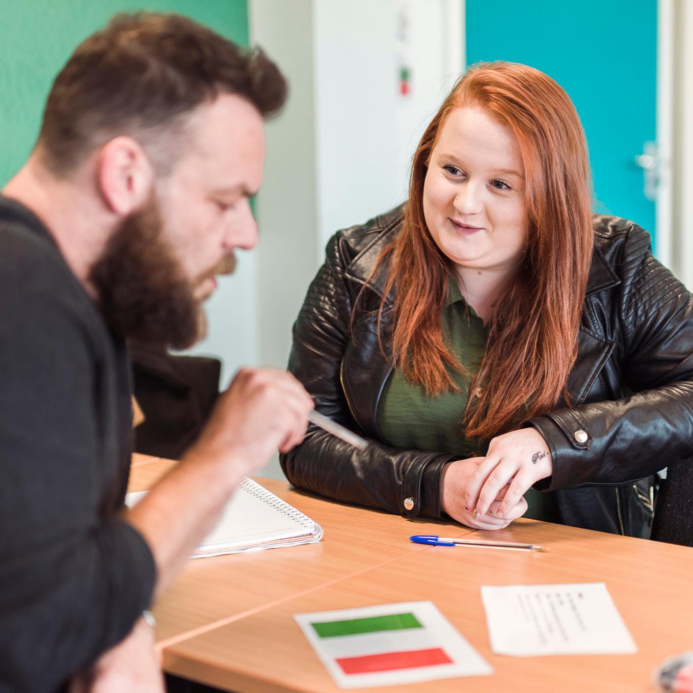 Health & Wellbeing students sit on opposite sides of a desk and discuss their work