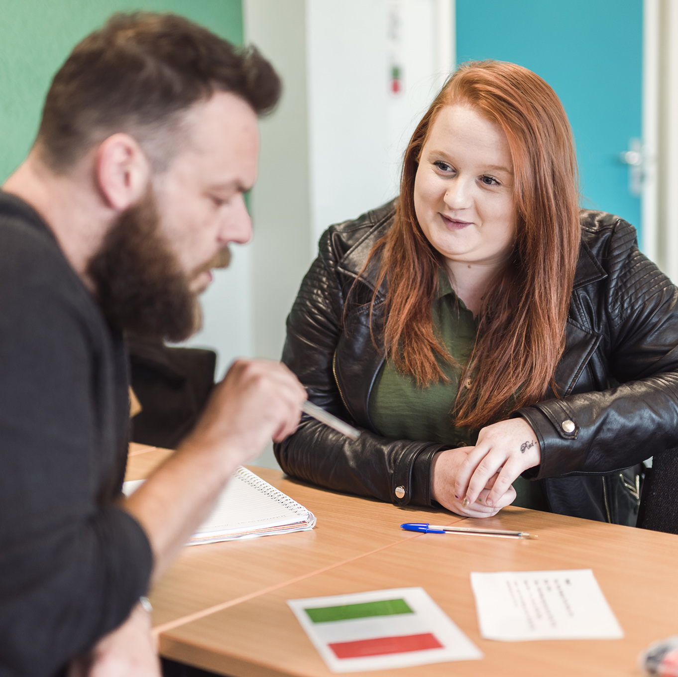 Health & Wellbeing students sit on opposite sides of a desk and discuss their work