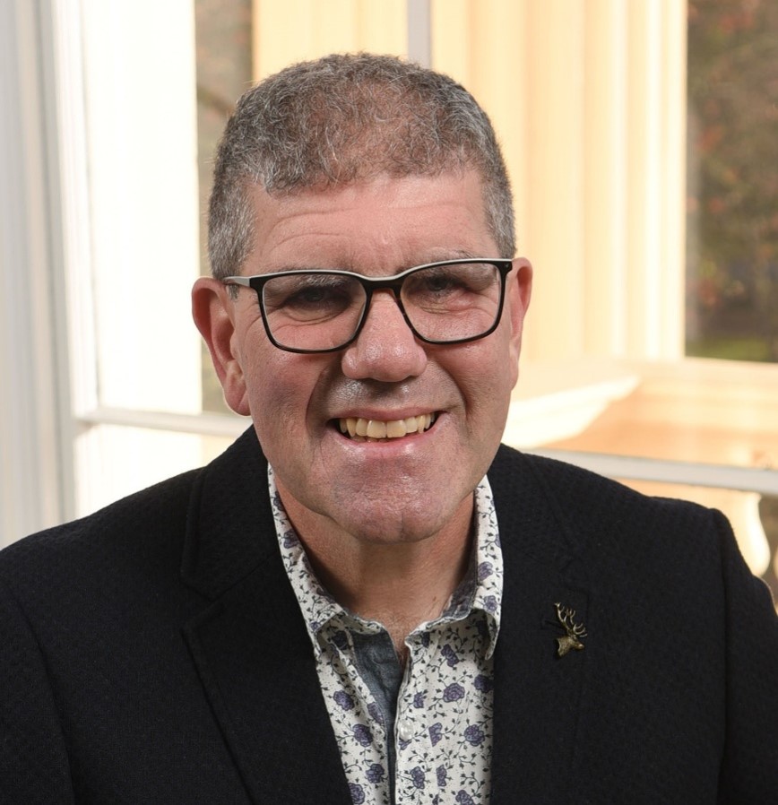 Head and shoulders shot of a professor with glasses in a shirt and jacket