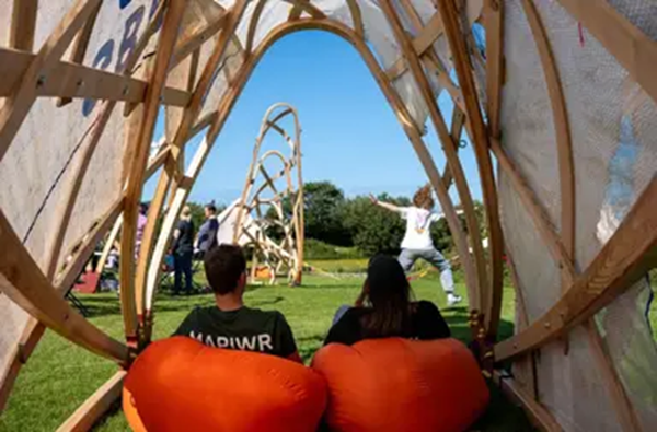 Back of two people sat on red beanbags outdoors on the grass watching other people