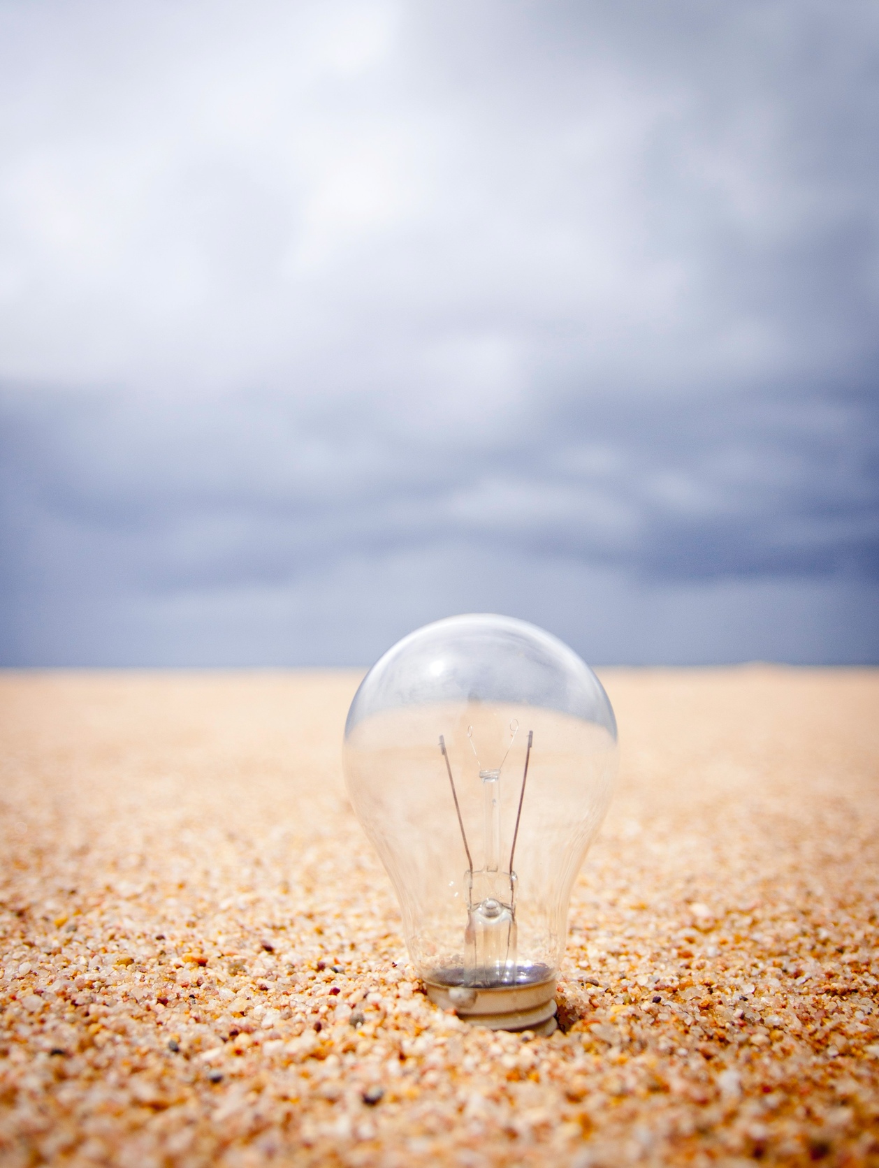 Light bulb in grains of sand on a beach with blue sky in the background