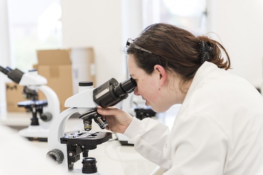 Student in a lab coat using a microscope