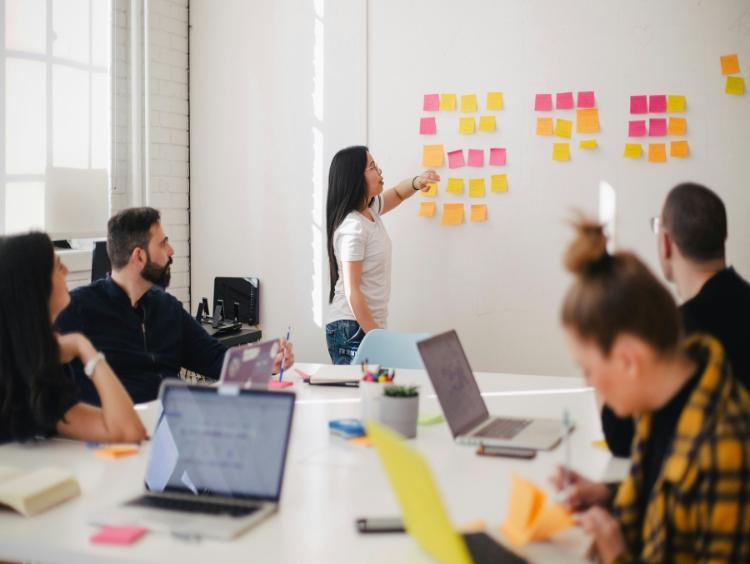 Group of colleagues working around a table with one colleague using post it notes on the wall