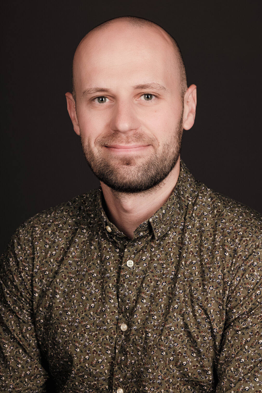 Head and shoulders professional shot of adam smiling wearing a brown patterned shirt