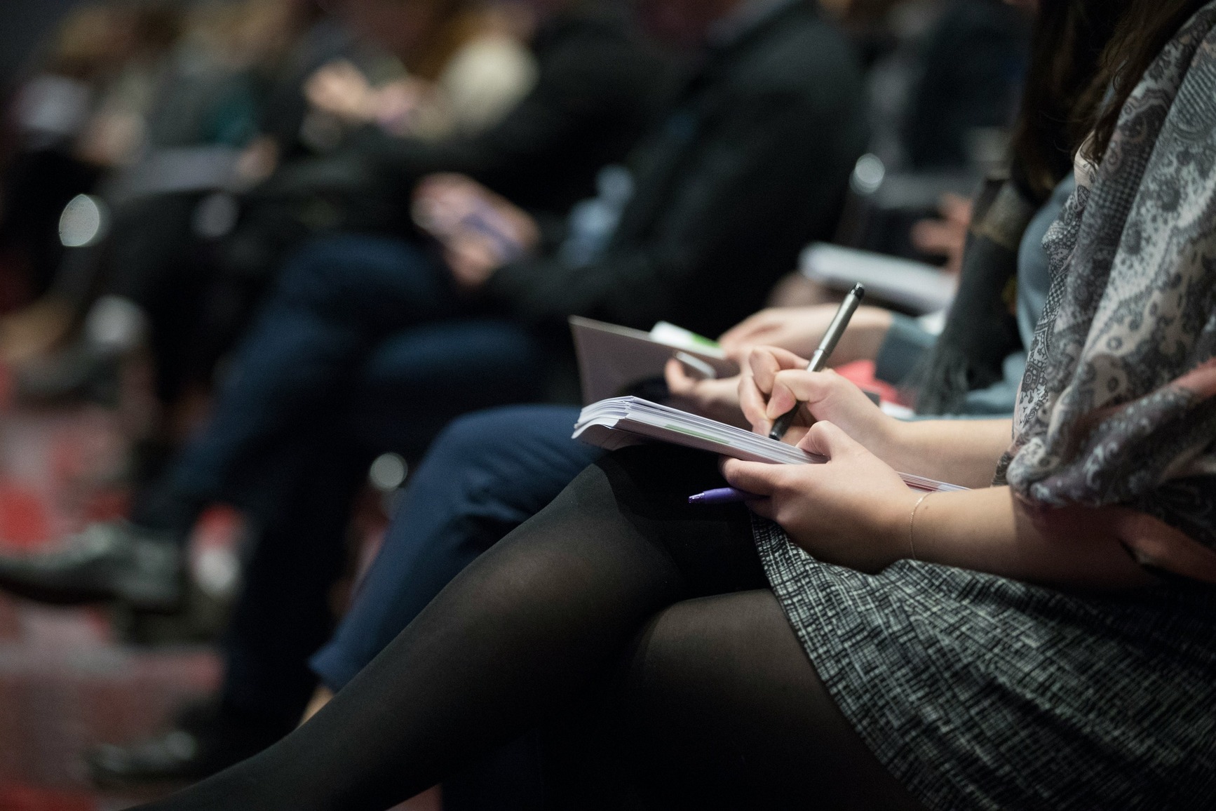 People sat down taking notes at a conference with only legs and arms in the image