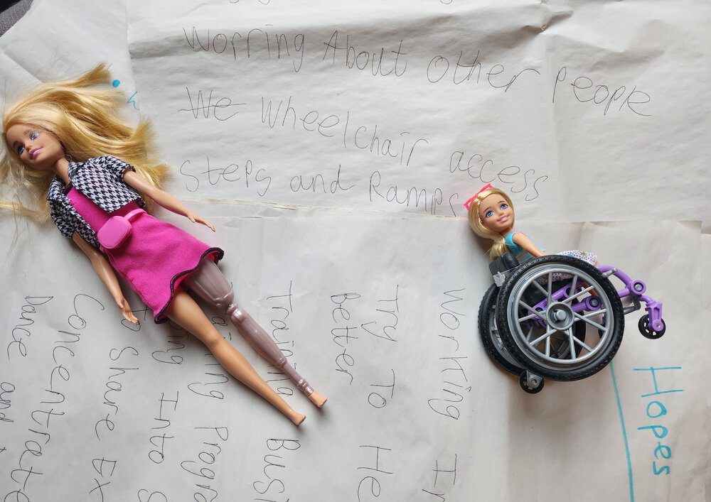 two barbie dolls, one in a wheelchair on top of flipchart paper