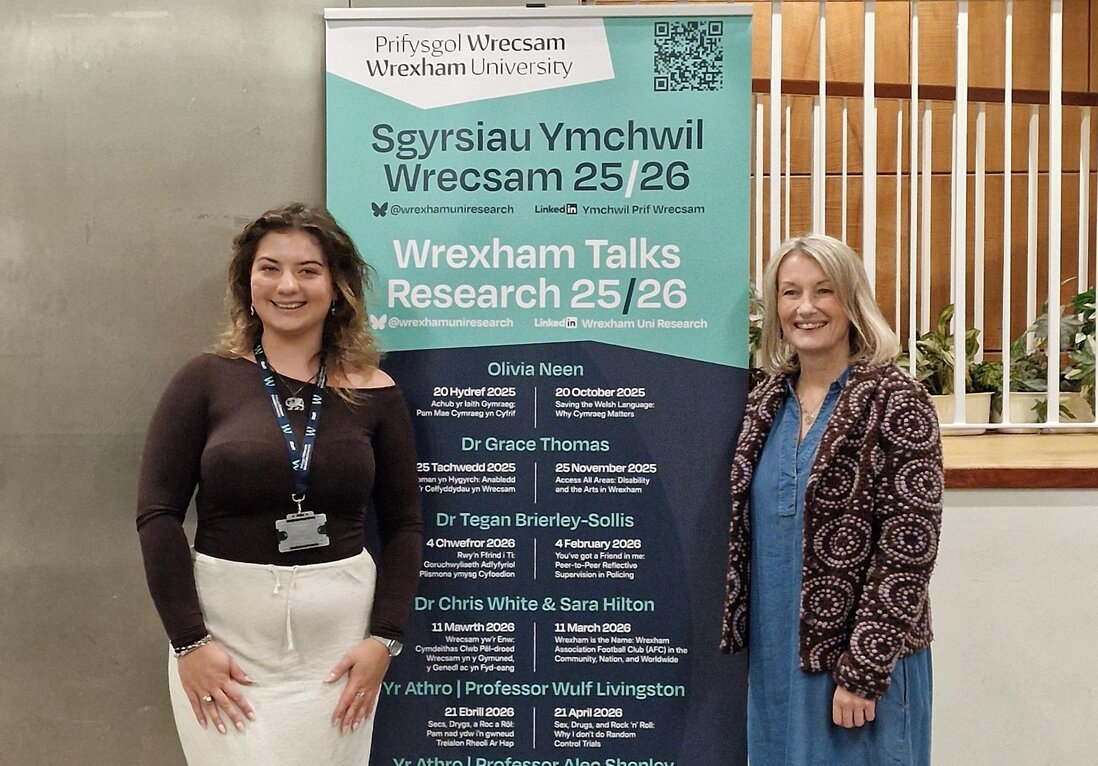 Olivia and Elen Mai standing by a banner