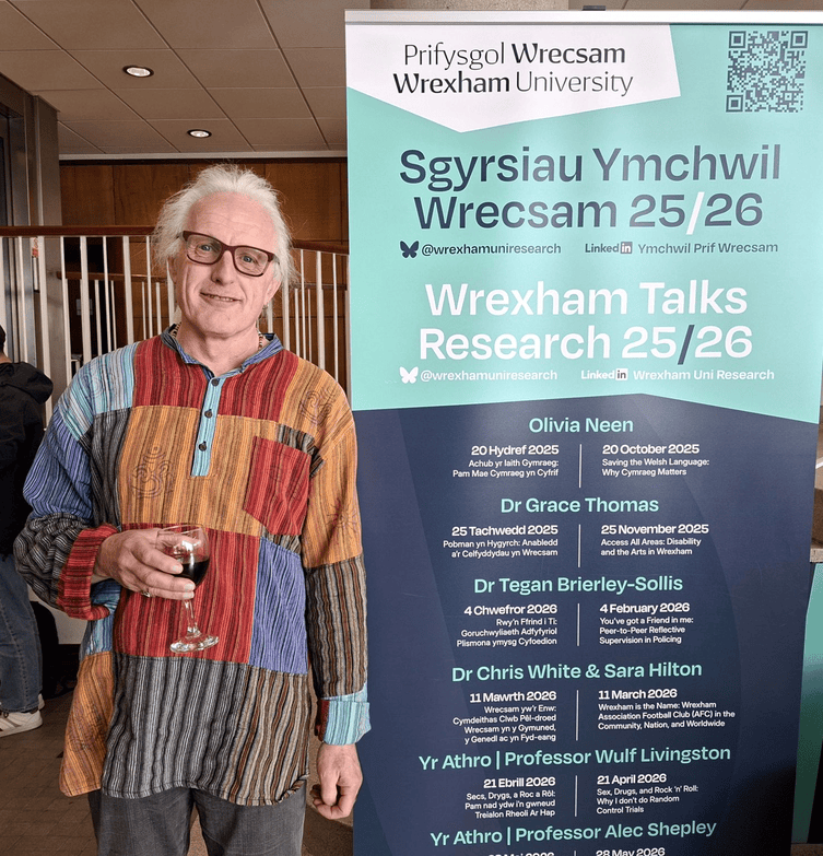 Prof. Wulf standing next to a banner with a drink in hand